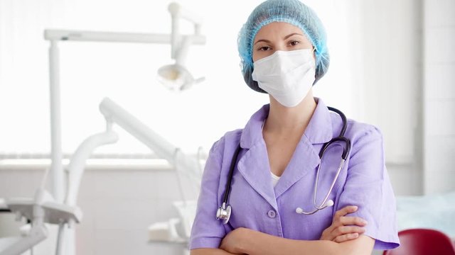 Portrait of confident professional female doctor standing in hospital room with arms crossed. Woman physician in medical mask and cap with stethoscope at work. Health care concept