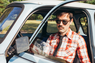 Portrait of Young Man Sitting in Blue Vintage Car and Looking at Road Map