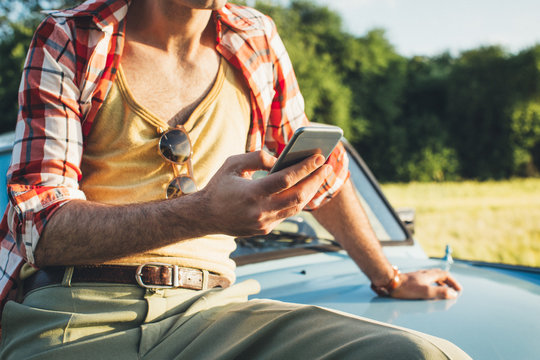 Retro-Styled Young Man Sitting on Blue Vintage Car and Typing on Cellphone