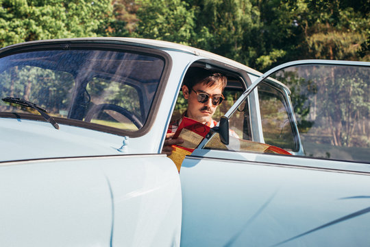 Young Man Sitting in Blue Vintage Car and Studying Road Map
