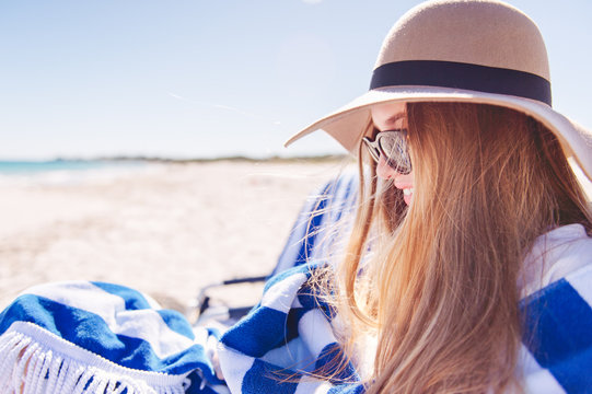 Smiling teenage girl wearing hat and sunglasses and wrapped in a towel at the beach on a sunny day