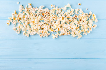 Popcorn horizontal banner. Red stripped paper cup and kernels lying on blue wooden background. Copy space. Top view.