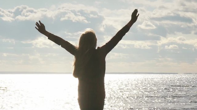 girl on the beach raises his arms to the sky
