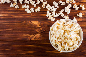 Popcorn horizontal banner. Red stripped paper cup and kernels lying on dark brown wooden background. Copy space. Top view.