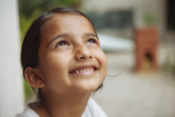 A young south asian girl smiling and looking up.