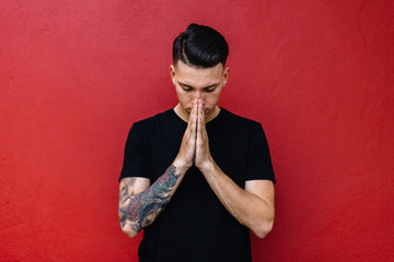 Man with tattoos prayer against a red wall
