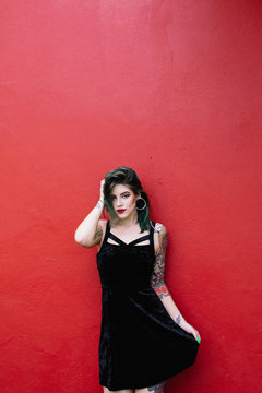 Portrait of a woman with tattoos and piercing against a blood red wall