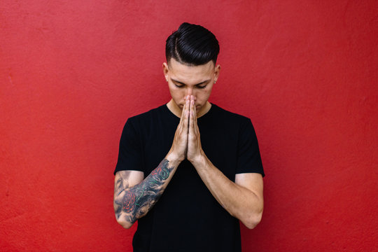 Man with tattoos prayer against a red wall