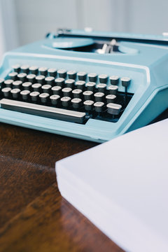 blue typewriter with a ream of blank paper