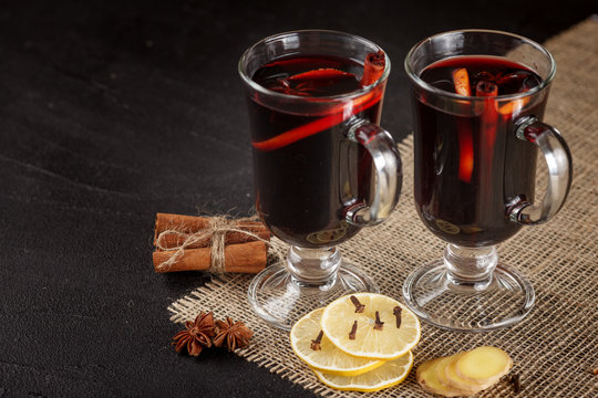 Mulled wine banner. Glasses with hot red wine and spices on dark background. Modern dark mood style.