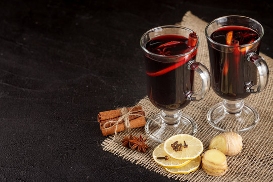 Mulled wine banner. Glasses with hot red wine and spices on dark background. Modern dark mood style.