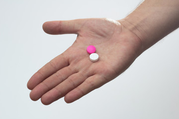 hand holding white and pink pills against white background
