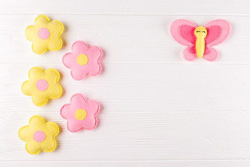 Craft pink and yellow butterfly and flowers, copyspace on white wooden background. Hand made felt toys. Abstract sky.
