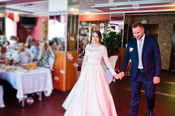 Beautiful wedding couple performing their first dance in the restaurant with different lights and bubbles and guests on the background.