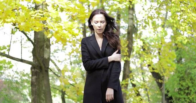 Attractive sad woman in black jacket feeling cold and keeping her arms crossed while walking in autumn park.