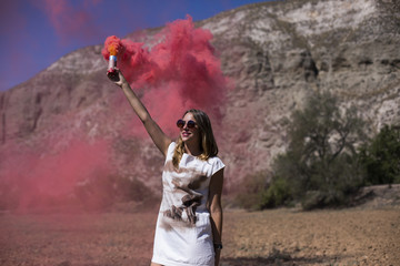close up view of a young beautiful woman holding a red smoke bomb outdoors. Sunny. Casual clothing. Lifestyle