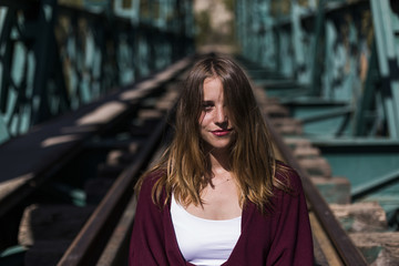 portrait of a young beautiful woman sitting on the railway and looking at the camera. Hair covering half of her face.LIfestyle. Outdoors. Sunny