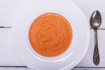 pumpkin soup in a white round plate and an iron spoon