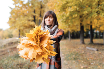 Autumn girl walking in city park. Portrait of happy lovely and beautiful young woman in forest in fall colors. Focus on the bouquet