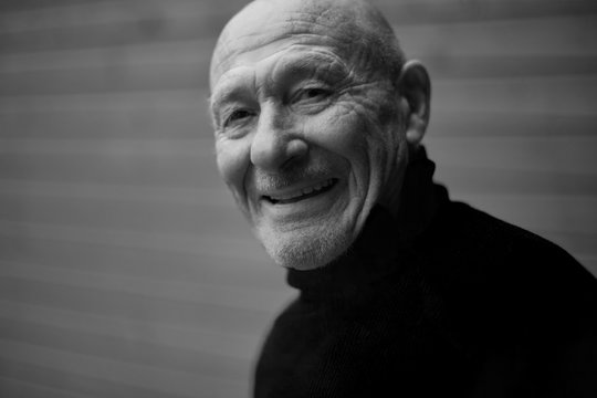 .Black and white horizontal capture of handsome happy senior expressing positivity and young soul, playing with camera and laughing. Old senior man closeup portrait. People, feelings, human concept.