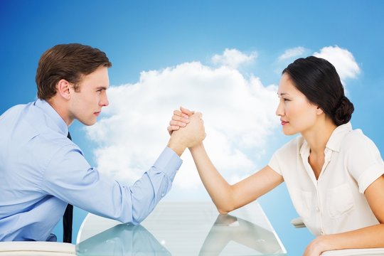 Composite image of business couple arm wrestling at desk
