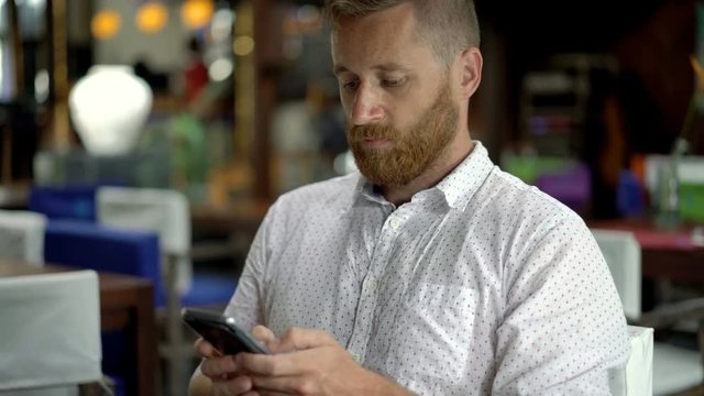 Handsome man sitting in restaurant and texting on smartphone, steadycam shot
