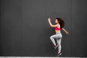 Sport fitness girl in fashion sportswear jumping in the street, on gray wall background ,outdoor sports. Urban style.