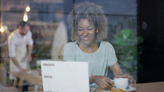 Young woman using laptop in a cafe with coffee & croissant