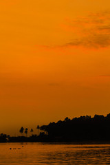 After sunset orange glow over the sun and sea, with silhouette of an island behind