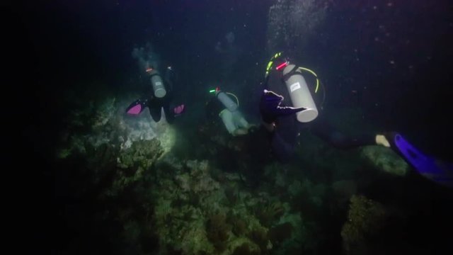 Group of scuba divers exploring deep dark ocean with flashlights