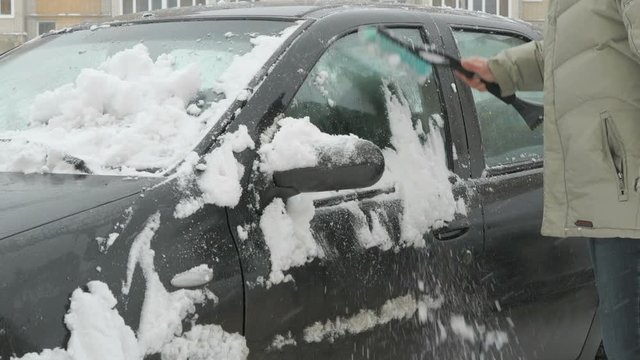 Caucasian man is cleaning black car from snow during snowfall in the yard