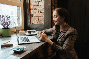 Young attractive woman sitting in a cafe in the morning before her work and planning tasks for the whole day. Beautiful lady talking on the phone and discussing business strategies with her colleague.