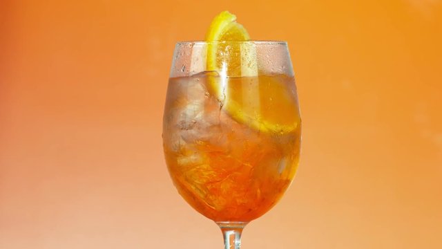 Colorful iced summer drink in a glass on orange background, slow motion