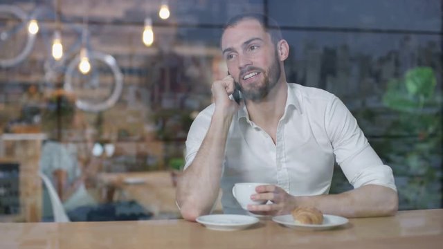 Young man talking on phone in cafe & looking out of the window