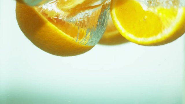 Fresh sliced lemons dropping into clear pure water, close up and in slow motion