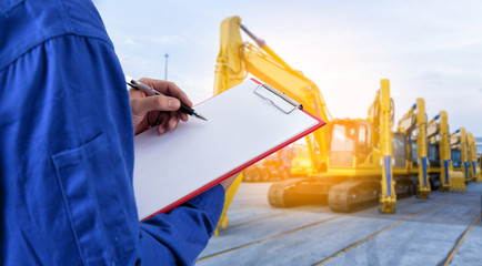 Worker checking document in front of the mechanical excavator at yard for import export business.