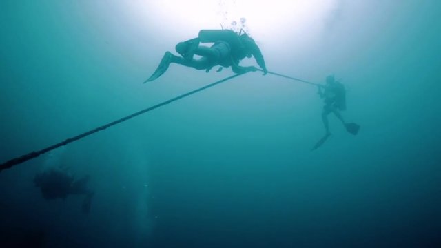 Scuba divers descending down a long rope from a boat into the ocean