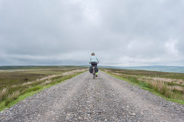 Female cyclist traveling across Northumberland moorland on the UK Coast to Coast cycle route