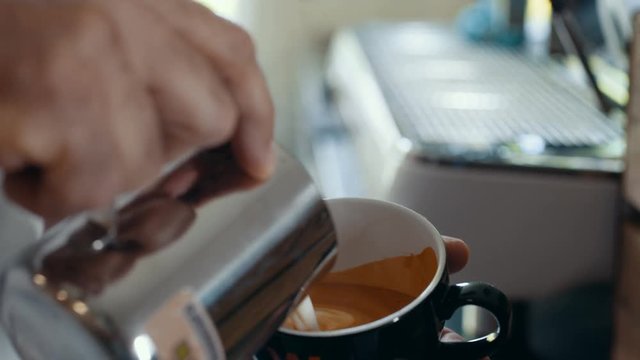  Close up hands of barista preparing coffee & creating pattern in the froth