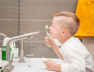 Happy boy looks at his teeth in the mirror after cleaning