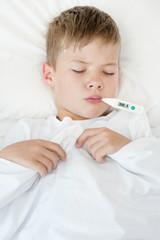 Sick boy with thermometer in mouth lying in bed