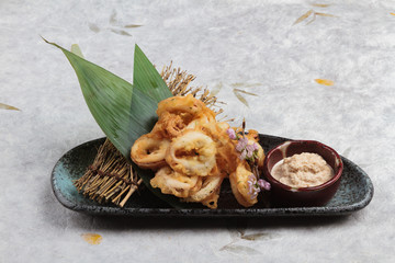 Japanese deep fried squid mixing tempura flour (Squid Karaage) served with sauce in black plate washi (Japanese paper). 