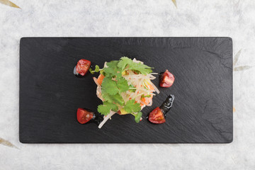 Top view of Diced salmon salad with avocado, tomato, onion, chilli, and coriander served in black rectangle stone plate on washi (Japanese paper). 