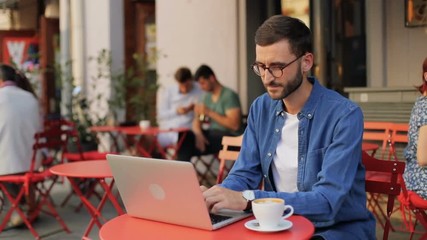 A portrait of a handsome young man working on a modern laptop in the cafe outdoors - Powered by Adobe