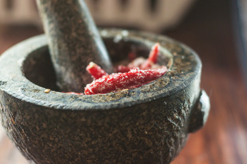 Cooking spicy thai sauce with chili pepper and sugar in Stone mortar with pestle on wooden table
