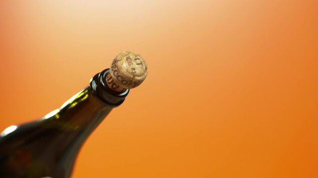  Sparkling wine cork popping from the bottle on orange background