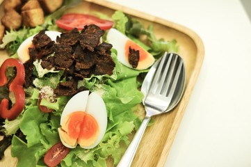 Caesar salad with croutons, boiled eggs, cherry tomatoes and fried bacon on top.