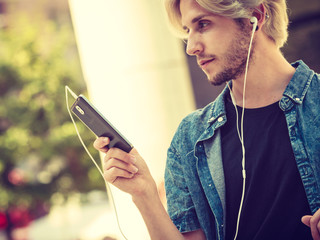 Hipster man standing on city street listening music