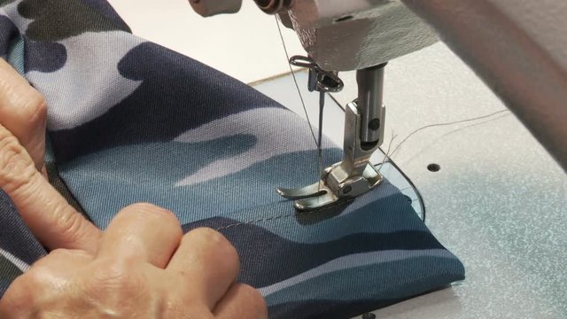 Close-up of a woman's hand making a military uniform on a sewing machine