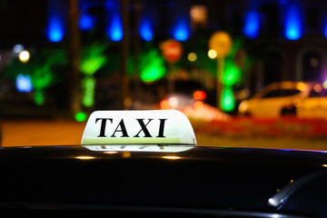 A glowing taxi sign on the roof of the car in the light of the lights of the night city.